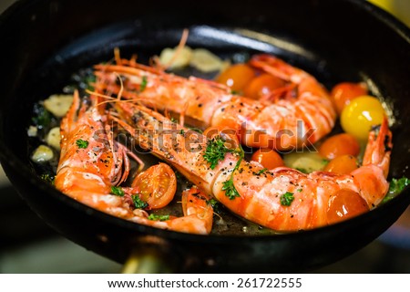 Shrimps on a cast iron skillet with cherry tomatoes in the restaurant. Process of cooking.