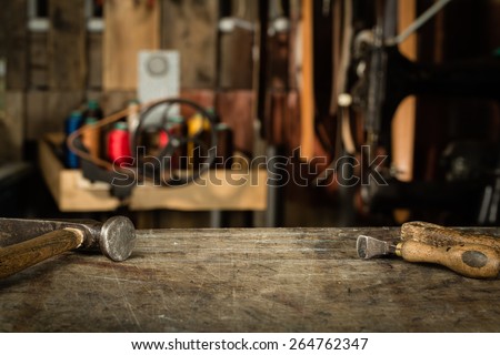 Leather crafting tools on working desk with the scratches. Blurred background of leather workshop. Copy space.