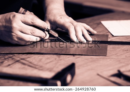 Working process of the leather wallet in the leather workshop. Woman's hands holding crafting tool and iron ruler. Monochrome cream tone. Black and white photography.