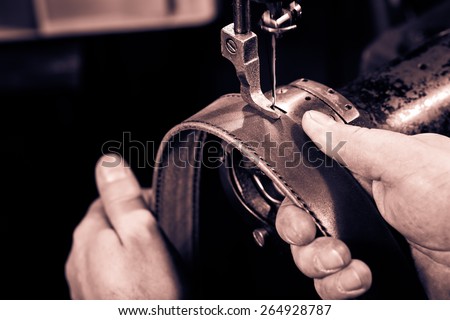 Sewing process of the leather belt. Man\'s hands behind sewing. Monochrome cream tone. Black and white photography.
