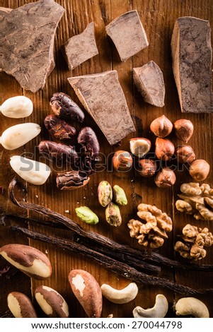 Raw cocoa mass with hazelnuts, walnuts, cashews and vanilla orchid pod on the grunge table or desk in the kitchen. Composition of the ingredients for cooking cakes or ice cream. View from above.