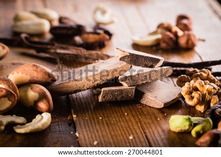 Raw cocoa mass with hazelnuts, walnuts, cashews and vanilla orchid pod on the grunge table or desk in the kitchen. Composition of the ingredients for cooking cakes or ice cream.