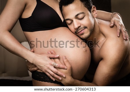 Happy and young pregnant couple hugging in the bedroom. Father listening to heartbeat of baby in mother\'s belly.