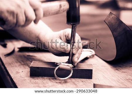 Process of making belt, creating leather belt with a low depth of field. Craftsman working with hammer.  Leather workshop. Black and white photography. Cream toned.