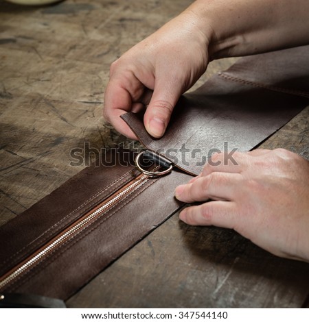 Working process of the leather bag or messenger in the leather workshop. Woman\'s hands holding the leather. Color tone image.