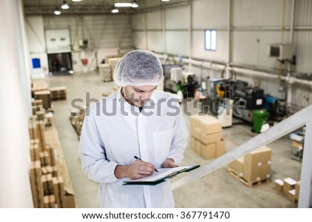 Worker In warehouse for food packaging. Manager writing on clipboard in automated production line at modern factory. View from above. Color toned image.