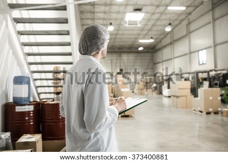 Worker In warehouse for food packaging. Manager writing on clipboard in automated production line at modern factory. Color toned image.