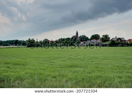 Rural landscape and town during weather change with heavy clouds and blue sky.