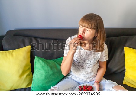 Young girl sitting on the couch and eating strawberries