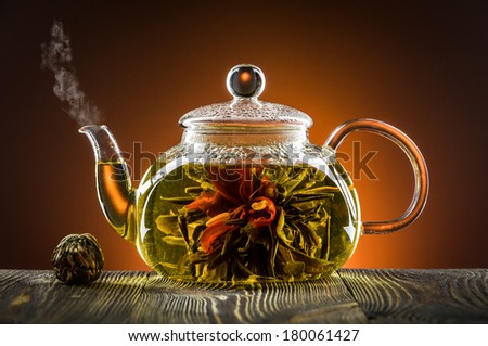 Glass teapot with blooming tea flower on wooden table