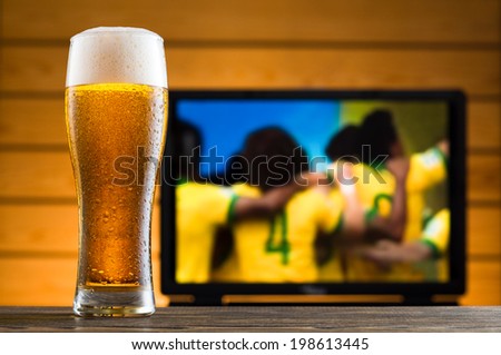 Glass of cold beer on the table, football match in background