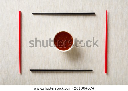 Chopsticks and bowl with sauce on table mat top view