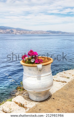 Colourful pink and white flowers in white clay pot overlooking the Saronic Gulf in Hydra island in the Aegean Sea, Greece.