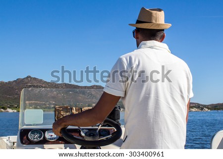 a man with a panama hat driving a boat near the coast