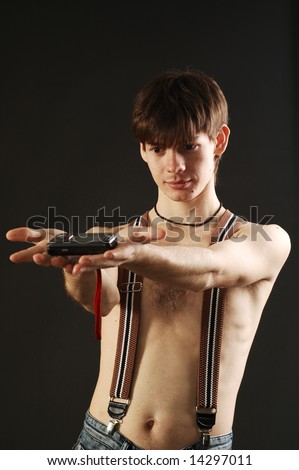 cute man  with nude torso wearing jeans with braces shows some electronic or cell phone