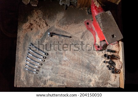 A set of wrenches, sockets and an anvil set on a flat view of a dusty workbench with a black background.