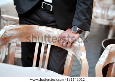 Black suit groom with hand and wristwatch on restaurant chair