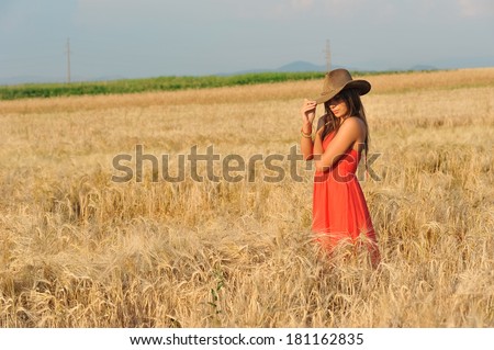 Beautiful woman with orange dress and hat standing in wheat field