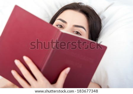 Closeup of young beautiful woman\'s eyes,reading a book in bed,standing on her back with her face covered by the book
