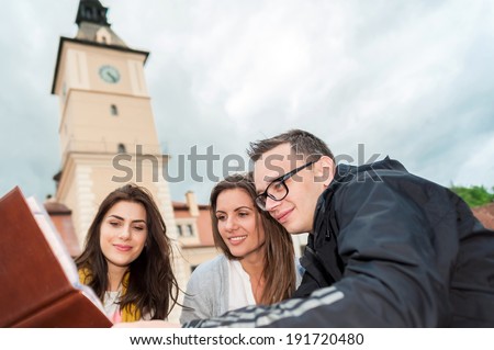 Cheerful group of friends, one man and two women sitting at the table, outdoor cafe shop, reading menu, talking having fun laughing smiling happy. In Brasov city.
