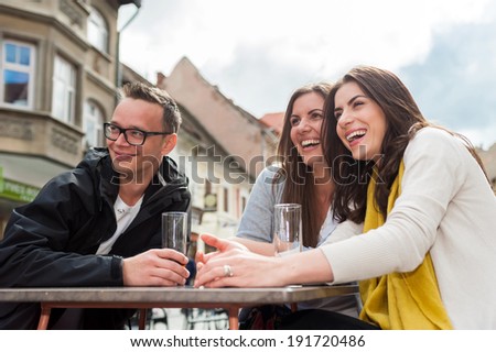 Cheerful group of friends, one man and two women sitting at the table, outdoor cafe shop, reading menu, talking having fun laughing smiling happy. In Brasov city.