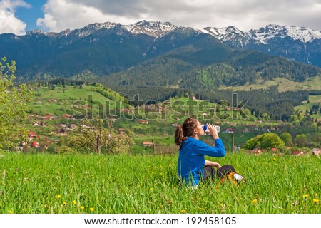 Hiking young woman resting and drinking water in the top of the mountain