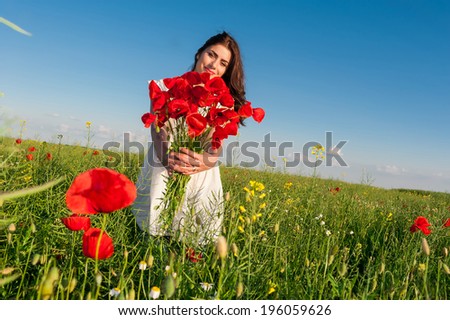 Beautiful young woman over Sky and Sunset in the field holding a poppies bouquet, smiling. Freedom concept. Series. Free Happy lady Enjoying Nature