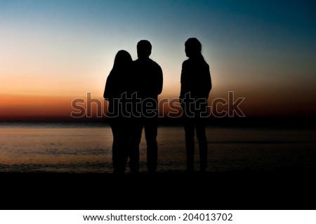 Silhouette of three friends in the morning at the beach waiting for the sunrise.
