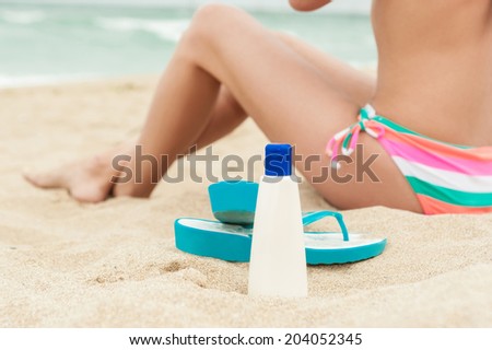 Woman applying sun protection lotion. Bottle of sun protection lotion and flip flops.