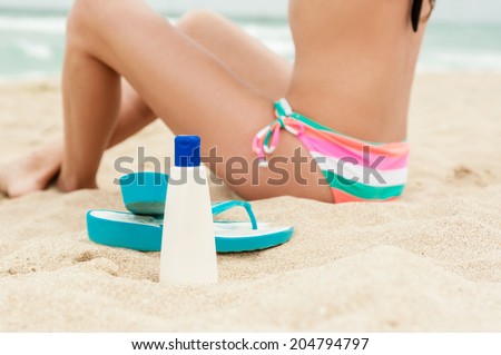 Woman applying sun protection lotion. Bottle of sun protection lotion and flip flops. Close-up, no face!