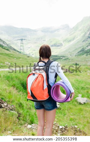 Woman sitting on mountain top admiring mountain landscape around and blue sky.