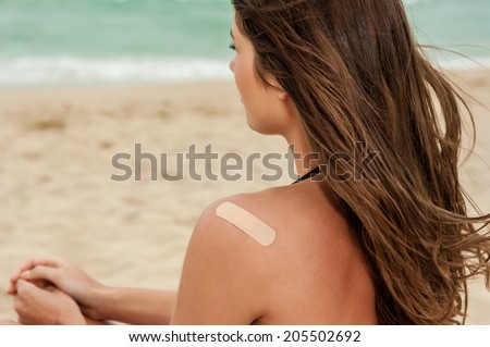 Woman at the beach with a on bandage her upper back.