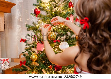 Close-up of pretty young woman in red and white christmas dress and long beautiful hair, decorating Christmas tree over living room.