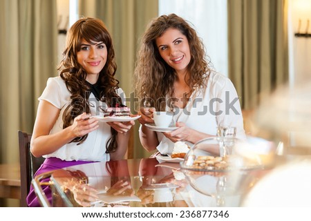 Two women chatting,smiling and having snack in coffee, enjoying a dessert, at the coffee / cake shop