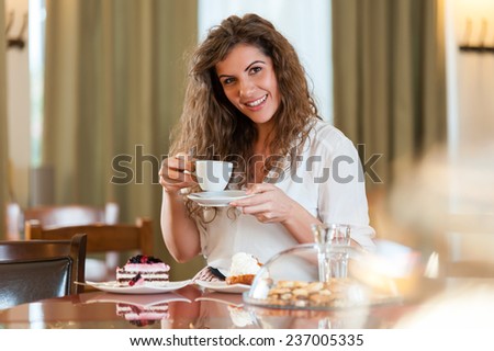Portrait of young pretty smiling woman enjoying fruit cake and coffee at the coffee / cake shop