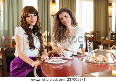 Two women chatting,smiling and having snack in caffee, enjoying a dessert, at the coffee / cake shop