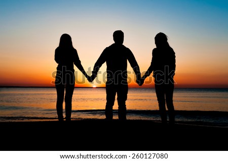 Silhouette of three friends in the morning at the beach  holding hands and looking at sunrise . Support, together, winning, helping, freedom concept.