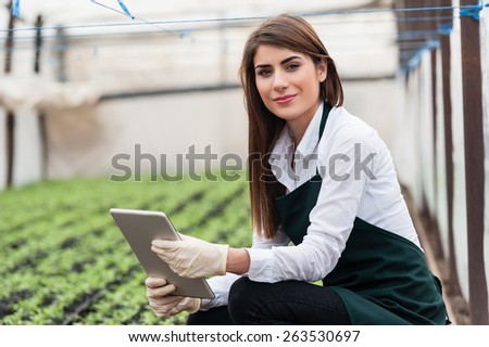 Female researcher technician studying with a tablet and gloves, dressed in office clothes,office shirt and apron in all withe greenhouse.
