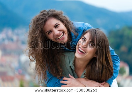 Two women friends laughing and hugging outdoors.