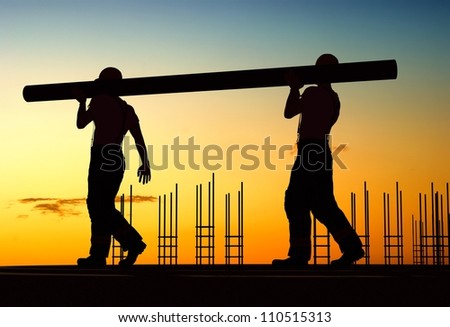 Two workers carry a pipe.