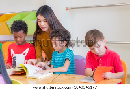 Asian female teacher teaching diversity kids reading book in classroom,Kindergarten pre school concept