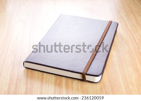 Brown Hard cover notebook with elastic strap on wooden table in perspective view,Template for adding your title