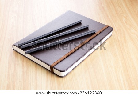 Three Black pencil on Brown Hard cover notebook with elastic strap on wooden table in perspective view