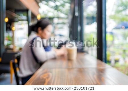 Blurred background : woman sitting at coffee shop with ice coffee on wooden table and see through shop window
