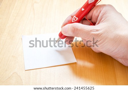 Hand holding red pen with white heart pattern, writing on blank notepad paper on wooden table,Template for adding your content,Love concept