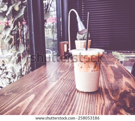 Vintage filter :Ice coffee on wood table beside window in coffee shop at garden