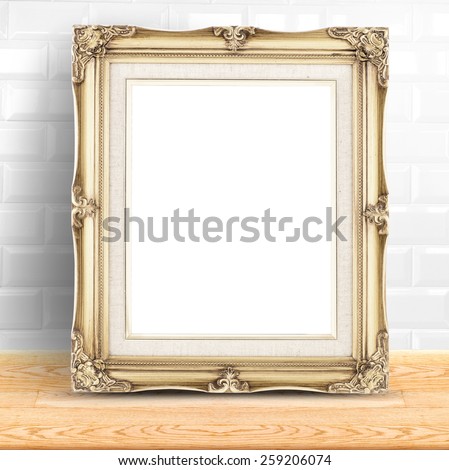Golden Vintage photo frame at white ceramic tiles wall and wooden table,Template mock up for display of product.