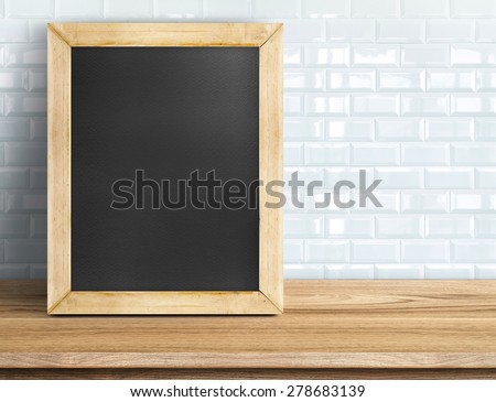 Blank blackboard on wooden table at white tile wall,Template mock up for adding your design and leave space beside frame for adding more text.