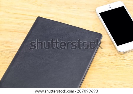 Close black blank notebook and mobile on wooden table,Mock up for adding your content , Clipping path on phone screen