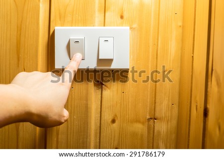 Finger press on light switch button at wooden wall